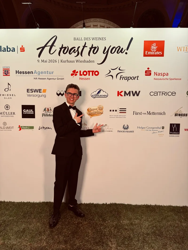 Luis Tillman zeigt beim Ball des Weines auf das Taunus Wunderland Logo an der Sponsorenwand